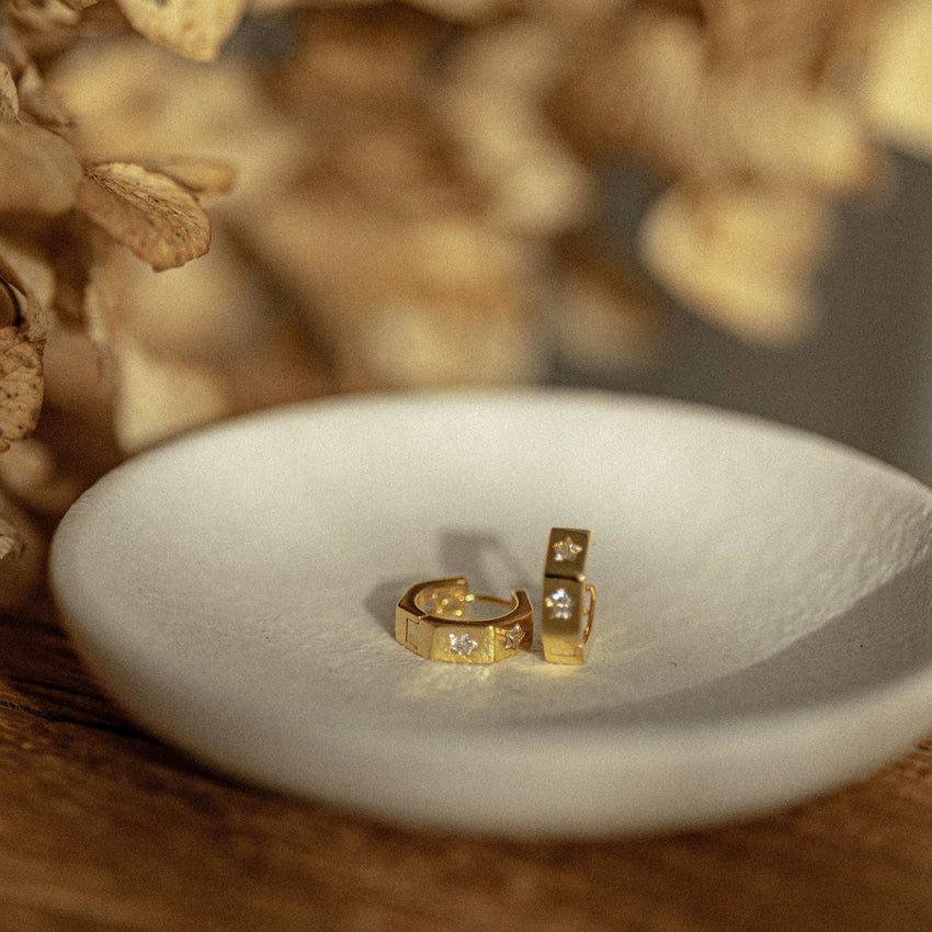 The Silver Linings Collective Whistledown Hoops in Gold on a textured bowl