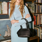 A model holding the Status Anxiety Astral Bag in Black on the short strap in front of a bookcase 