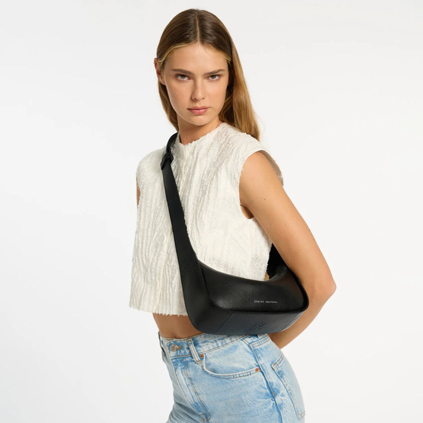 The Status Anxiety Haven Bag in Black on crossbody on a model on a grey background