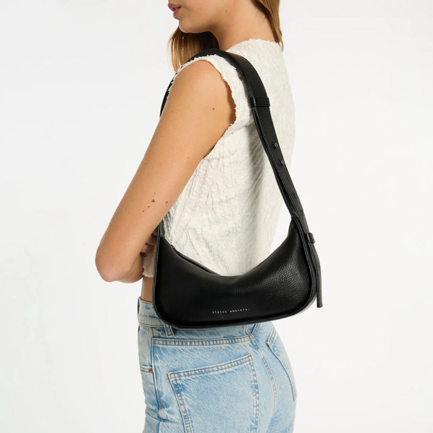 The Status Anxiety Haven Bag in Black on a models shoulder on a grey background