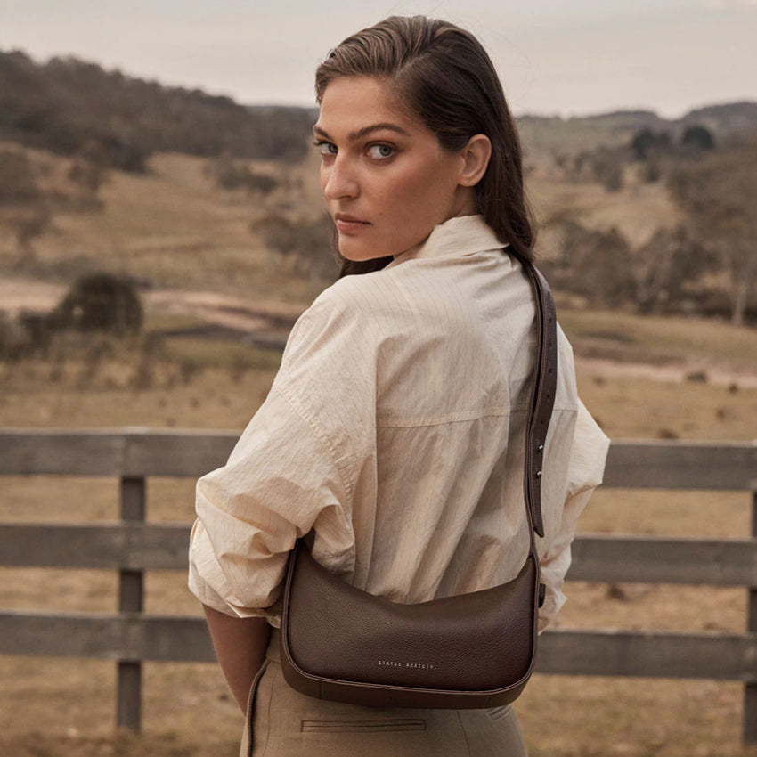 The Status Anxiety Haven Bag in Cocoa crossbody on a model in a paddock
