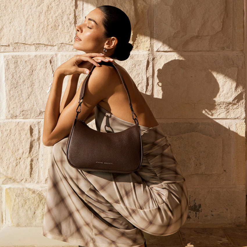 A model holding the Status Anxiety Look Both Ways Bag in Cocoa on her shoulder