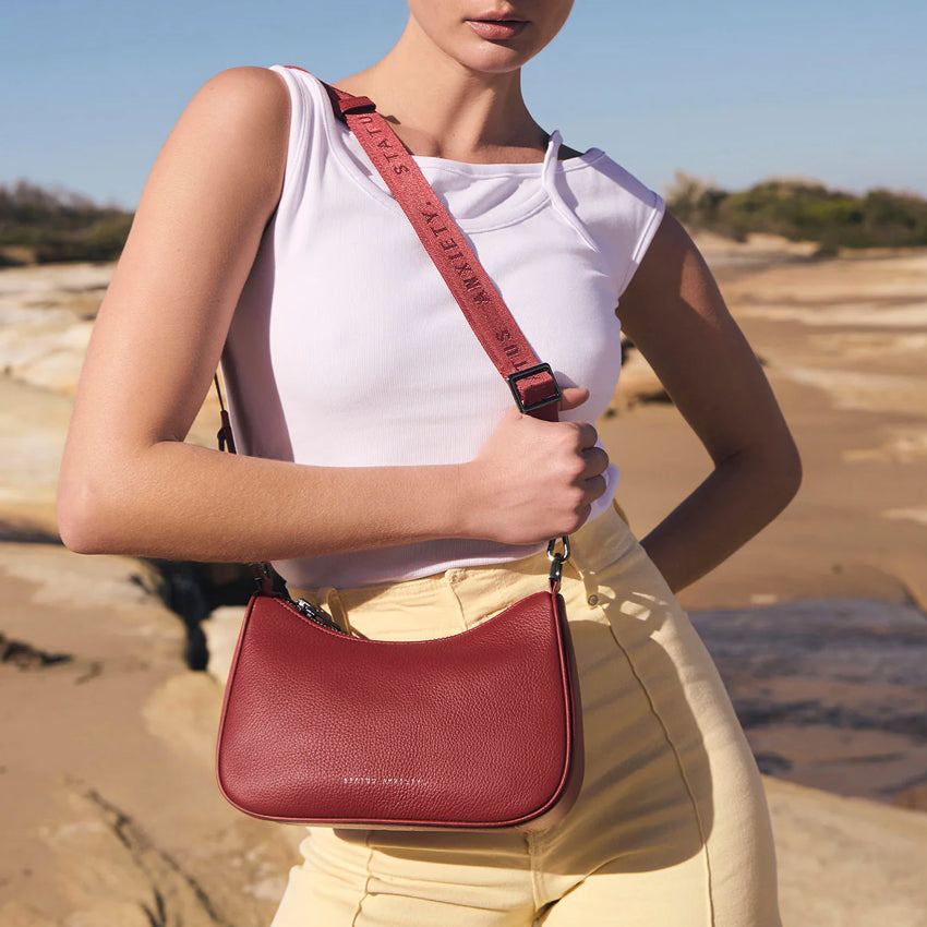 A model wearing the Status Anxiety Look Both Ways Bag in Rouge with the long webbed strap