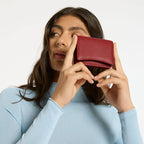 A model holding the Status Anxiety Lumen Wallet in Rouge up