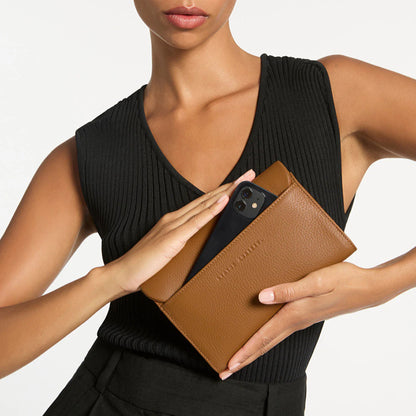 A model holding the Status Anxiety Remnant Wallet in Camel showing the back with a phone in it