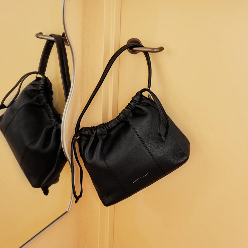The Status Anxiety Point Of No Return Bag  in Black hanging on a door handle