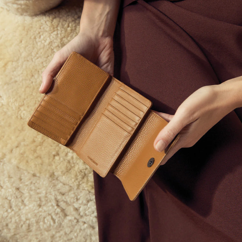 The Status Anxiety Visions Wallet in Tan with a model holding it open