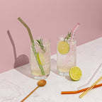 The Sucker Reusable Glass Straws in Multi  with two in drinks and 3 on the bench, with lime