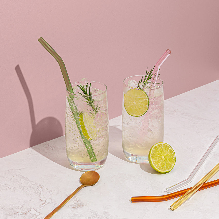 The Sucker Reusable Glass Straws in Multi  with two in drinks and 3 on the bench, with lime