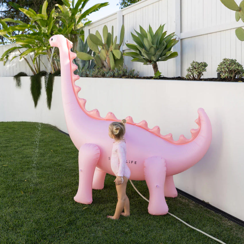 The SunnyLife Dino Giant Sprinkler in Pink with water coming out of it in a backyard