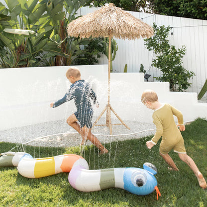 The Sunny Life Inflatable Snake Sprinkler in a yard with water coming out of it and kids running around it