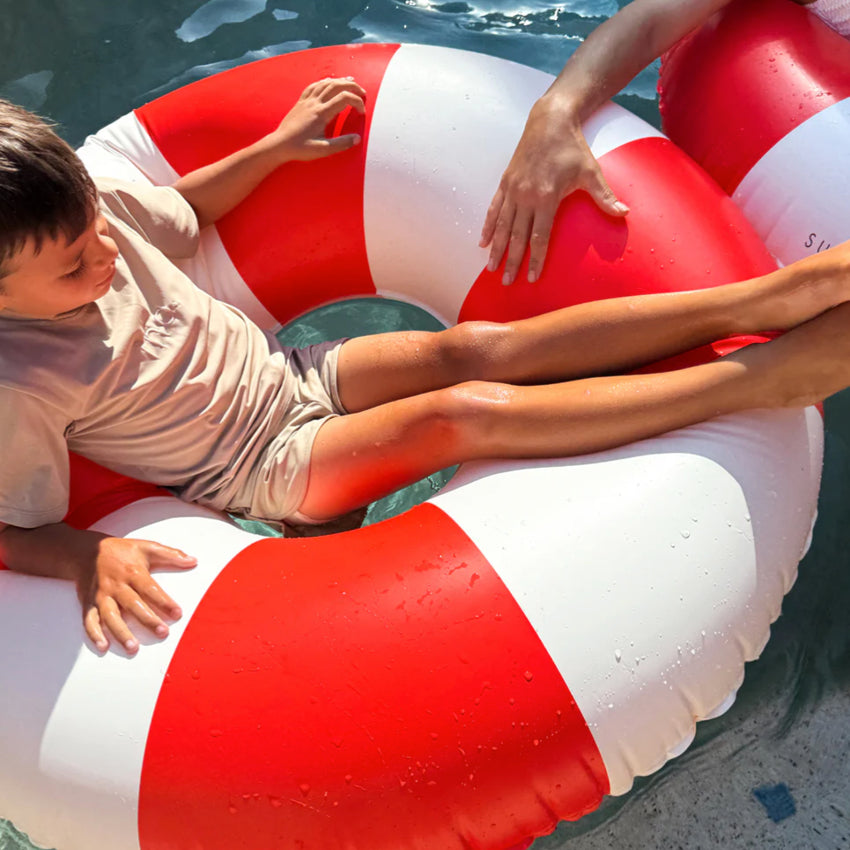 The Sunny Life Tube Pool Ring in Tomato Red Stripe in water with a kid in it