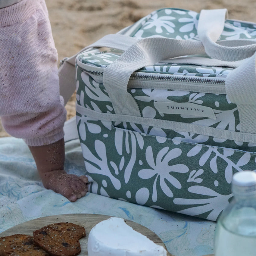 The Sunnylife Canvas Cooler Bag in Olive on a towel on the beach