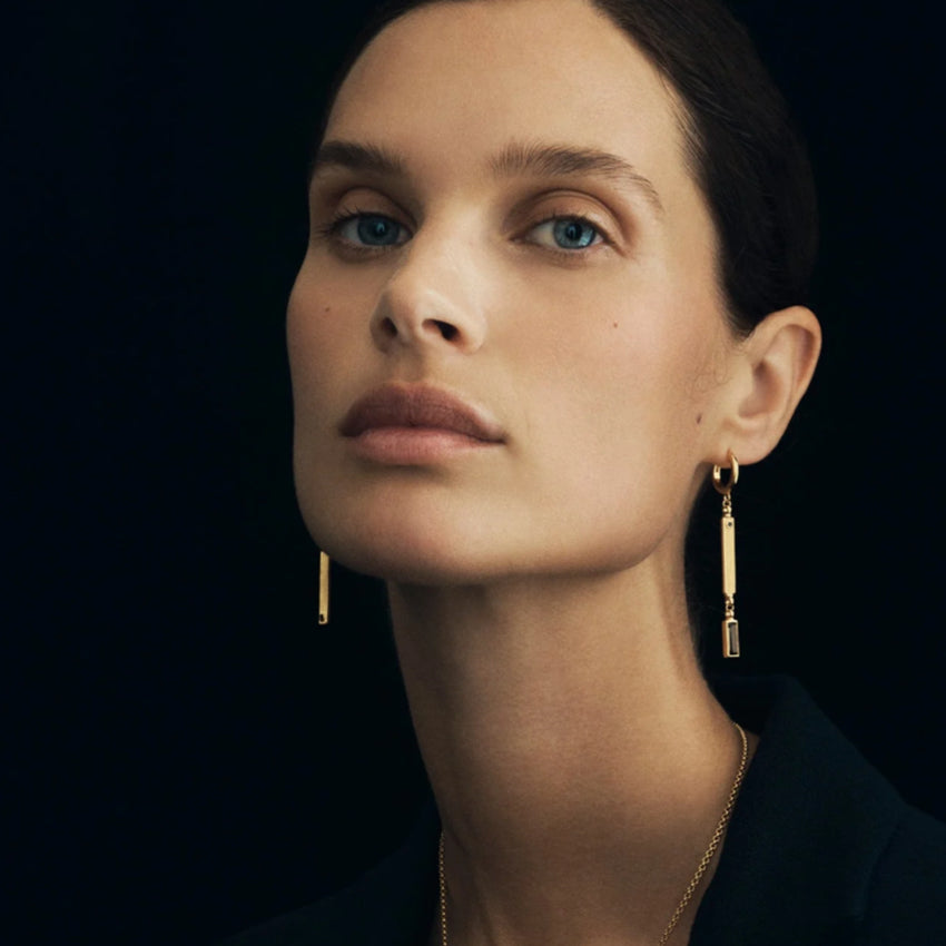The Temple Of The Sun Pele Earrings in Gold on a model with a dark background