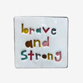 Square ceramic tile with 'brave and strong' text in multicolor on a white background