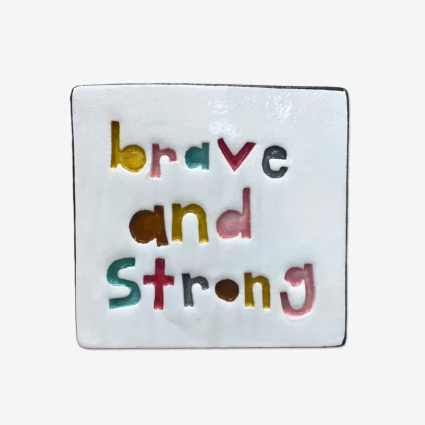 Square ceramic tile with 'brave and strong' text in multicolor on a white background