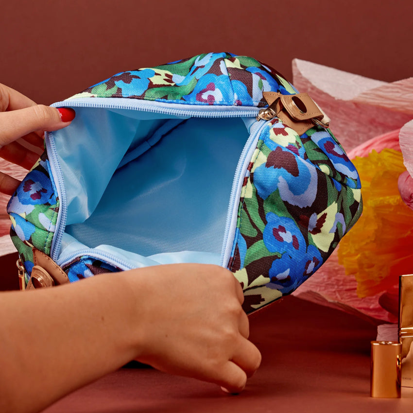 The Somewhere Co Cosmetic Bag in Pansy Path being opened next to craft flowers