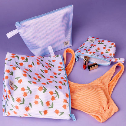 The Somewhere Co Handy Pouches in Sunburst with lipstick and bikini top coming out of them on a purple background