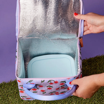 The Somewhere Co Lunch Bag in Sunburst being held open on a purple and grass background