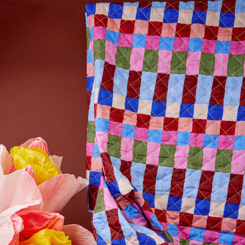 The Somewhere Co XL Picnic Rug in Hopscotch rolled out next to paper flowers