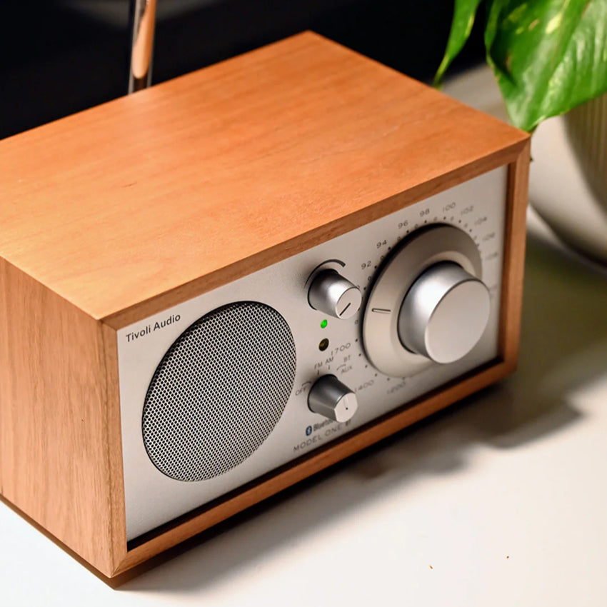 The Tivoli Audio Model One BT in Cherry and Silver on a table next to a pot plant