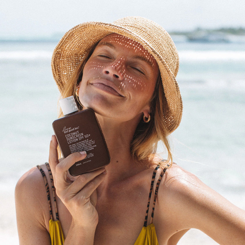 A model holding the We Are Feel Good Inc Coconut SPF50+ Sunscreen 200ml at the beach