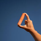 A hand holding up the We Are Feel Good Inc Signature SPF50+ Lip Balm to the sky