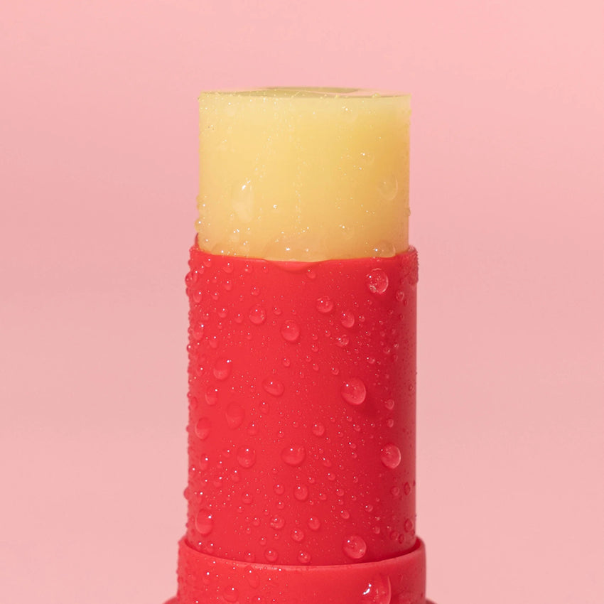 A closeup of the We Are Feel Good Inc Signature SPF50+ Lip Balm on a pink background