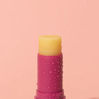 A closeup of the We Are Feel Good Inc Wild Rosella SPF 50+ Lip Balm on a pink background