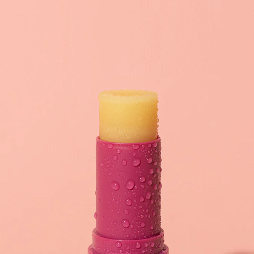 A closeup of the We Are Feel Good Inc Wild Rosella SPF 50+ Lip Balm on a pink background