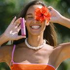 A model holding the We Are Feel Good Inc Wild Rosella SPF 50+ Lip Balm with a flower