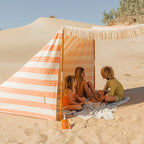 The We Are Feel Good Inc Sensitive SPF50+ Sunscreen Lotion 400ml on a the beach next to kids in a tent