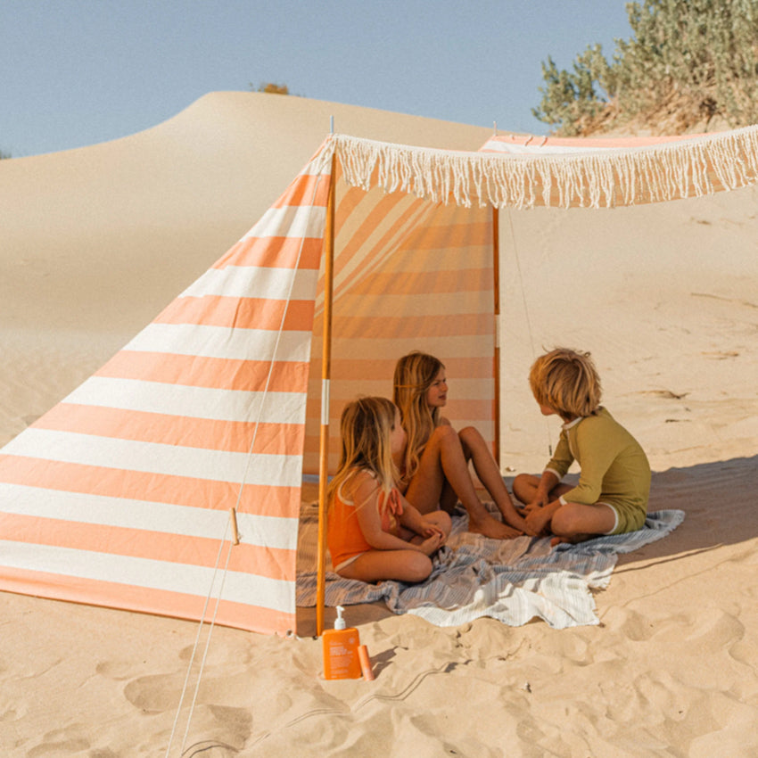The We Are Feel Good Inc Sensitive SPF50+ Sunscreen Lotion 400ml on a the beach next to kids in a tent