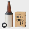 The Huski Beer Cooler in Champagne with a beer bottle in it next to its box on a blank background