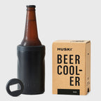 The Huski Beer Cooler in Black with a beer bottle in it next to its box on a blank background