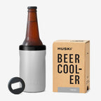 The Huski Beer Cooler in Stone Grey with a beer bottle in it next to its box on a blank background