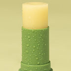 A closeup of the We Are Feel Good Inc Kakadu Plum SPF50+ Lip Balm on a green background