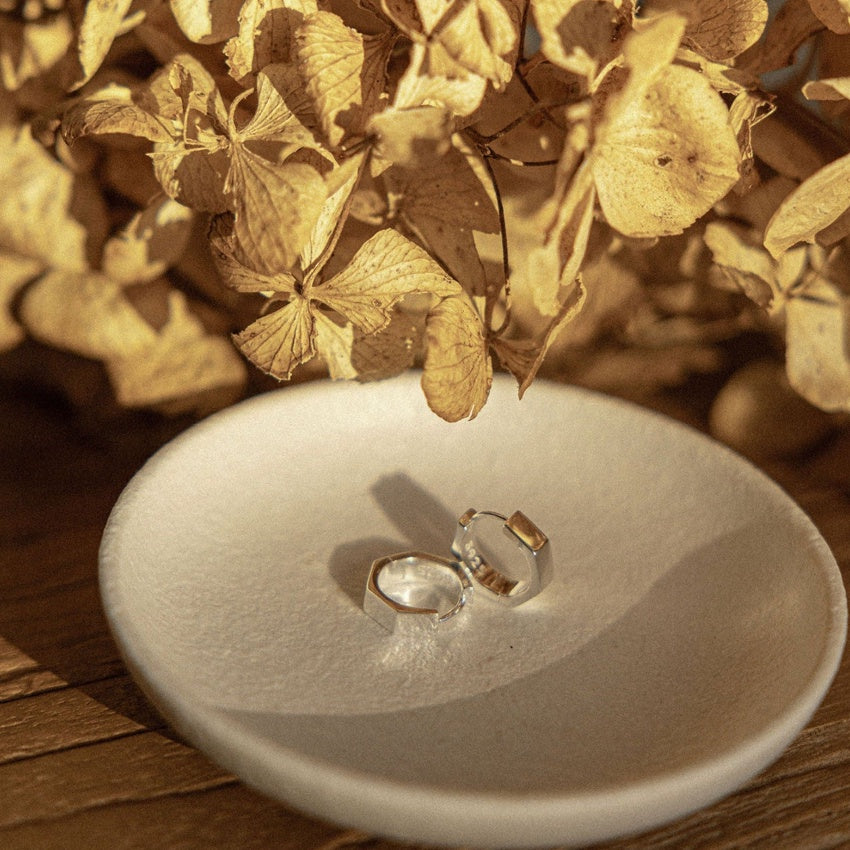 The Silver Linings Collective Whistledown Solid Hoops in Silver on a textured bowl with some flowers