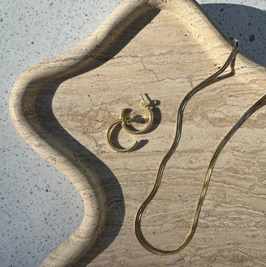 The Silver Linings Collective Navy Hoops in Gold on a textured tray next to a necklace