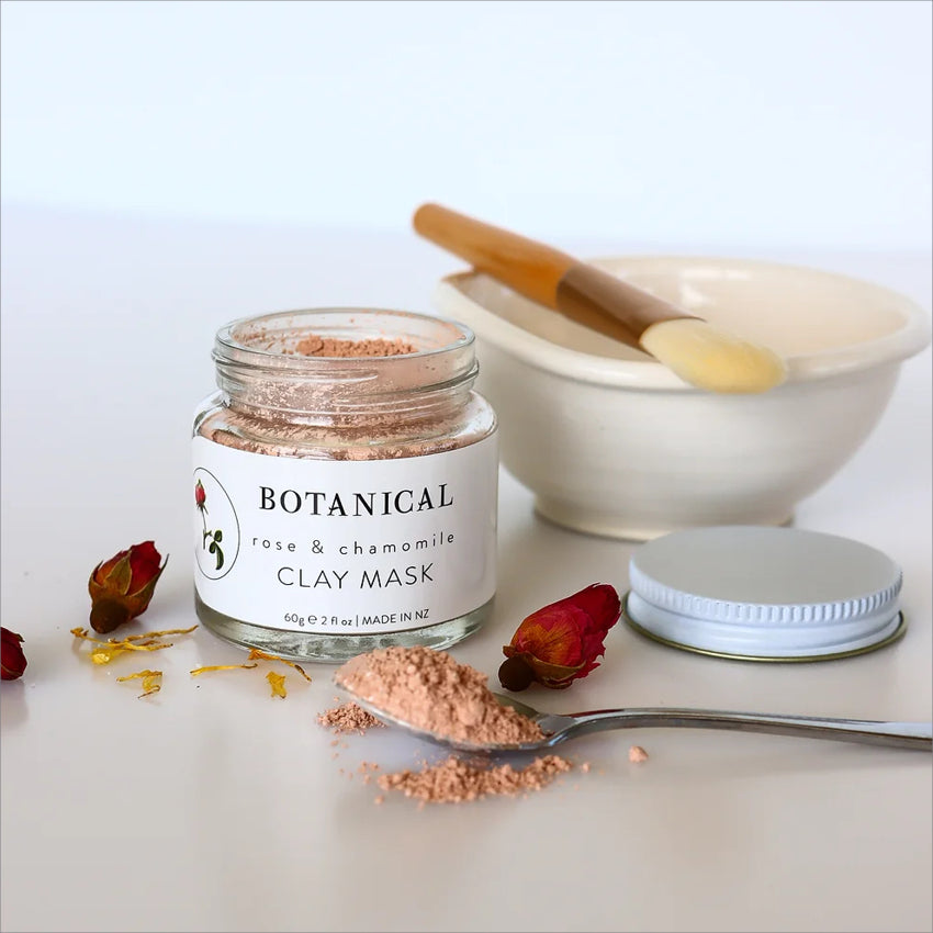 The Botanical Rose and Chamomile Clay Mask with the lid off next to a bowl and brush