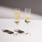 The Fazeek Wave Flute in Clear with champagne in them on a white table
