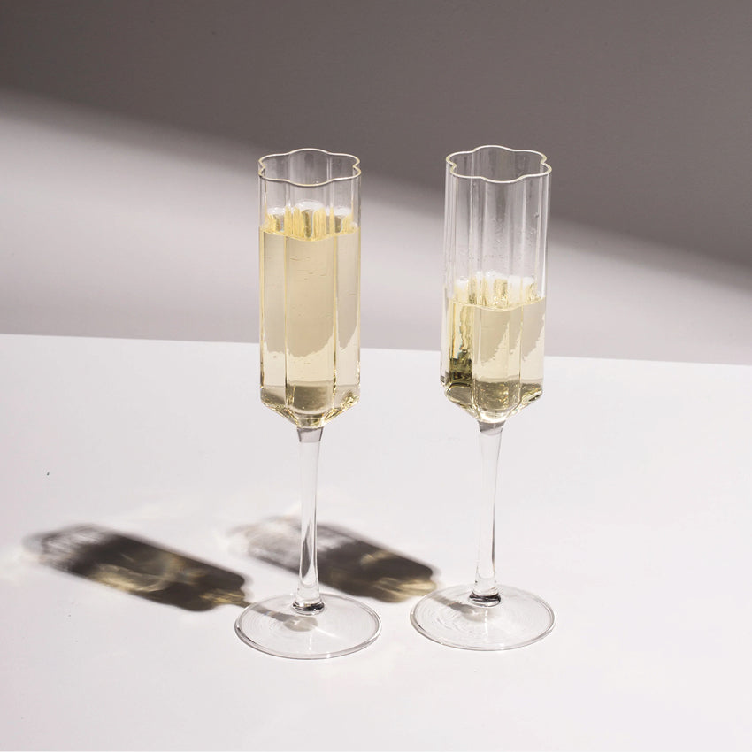 The Fazeek Wave Flute in Clear with champagne in them on a white table