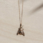 The Meadowlark Bee Charm Necklace in Gold suspended over a textured background.