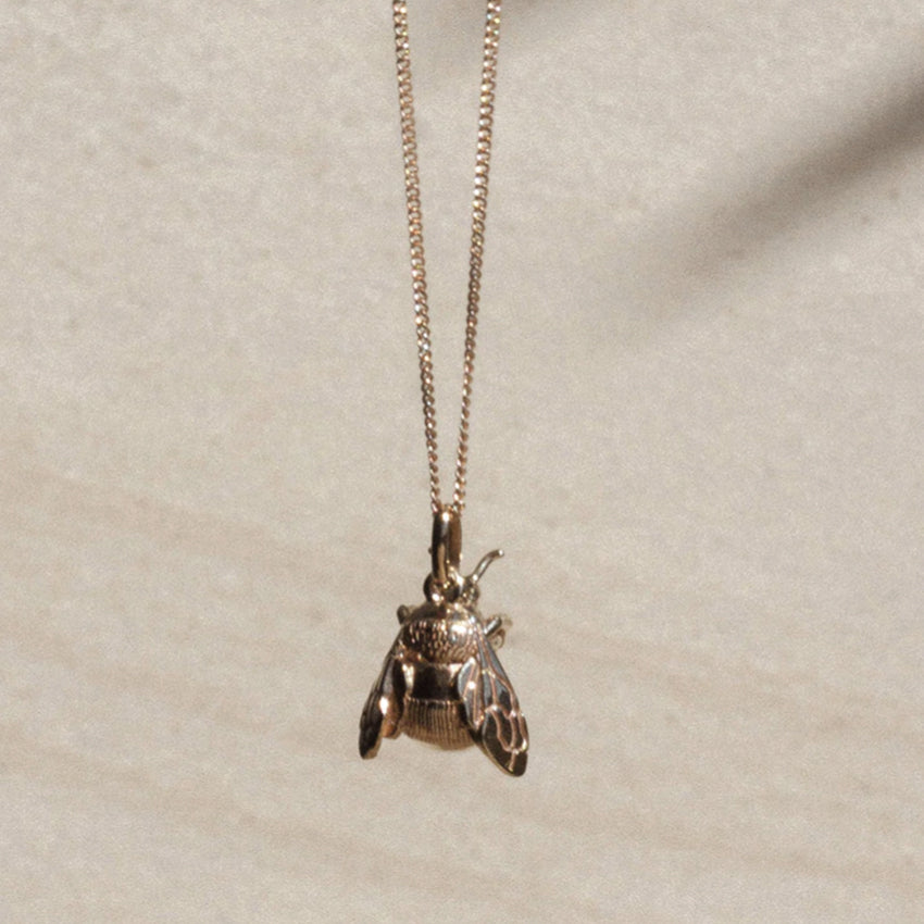 The Meadowlark Bee Charm Necklace in Gold suspended over a textured background.