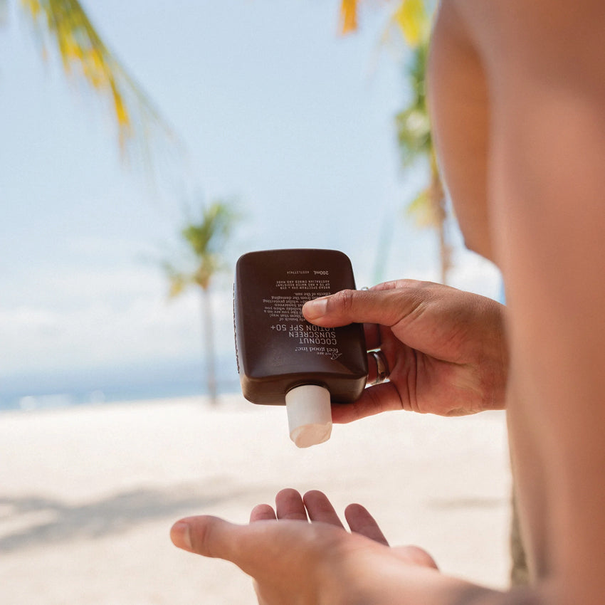 A model squirting the We Are Feel Good Inc Coconut SPF50+ Sunscreen in his hand on a beach