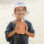 A kid holding the We Are Feel Good Inc Sensitive SPF50+ Sunscreen Lotion 400ml  on the beach