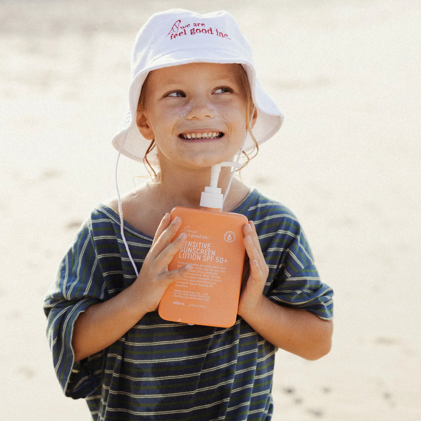 A kid holding the We Are Feel Good Inc Sensitive SPF50+ Sunscreen Lotion 400ml  on the beach