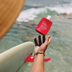 The We Are Feel Good Inc Signature SPF50+ Sunscreen Lotion 200ml being thrown by the sea